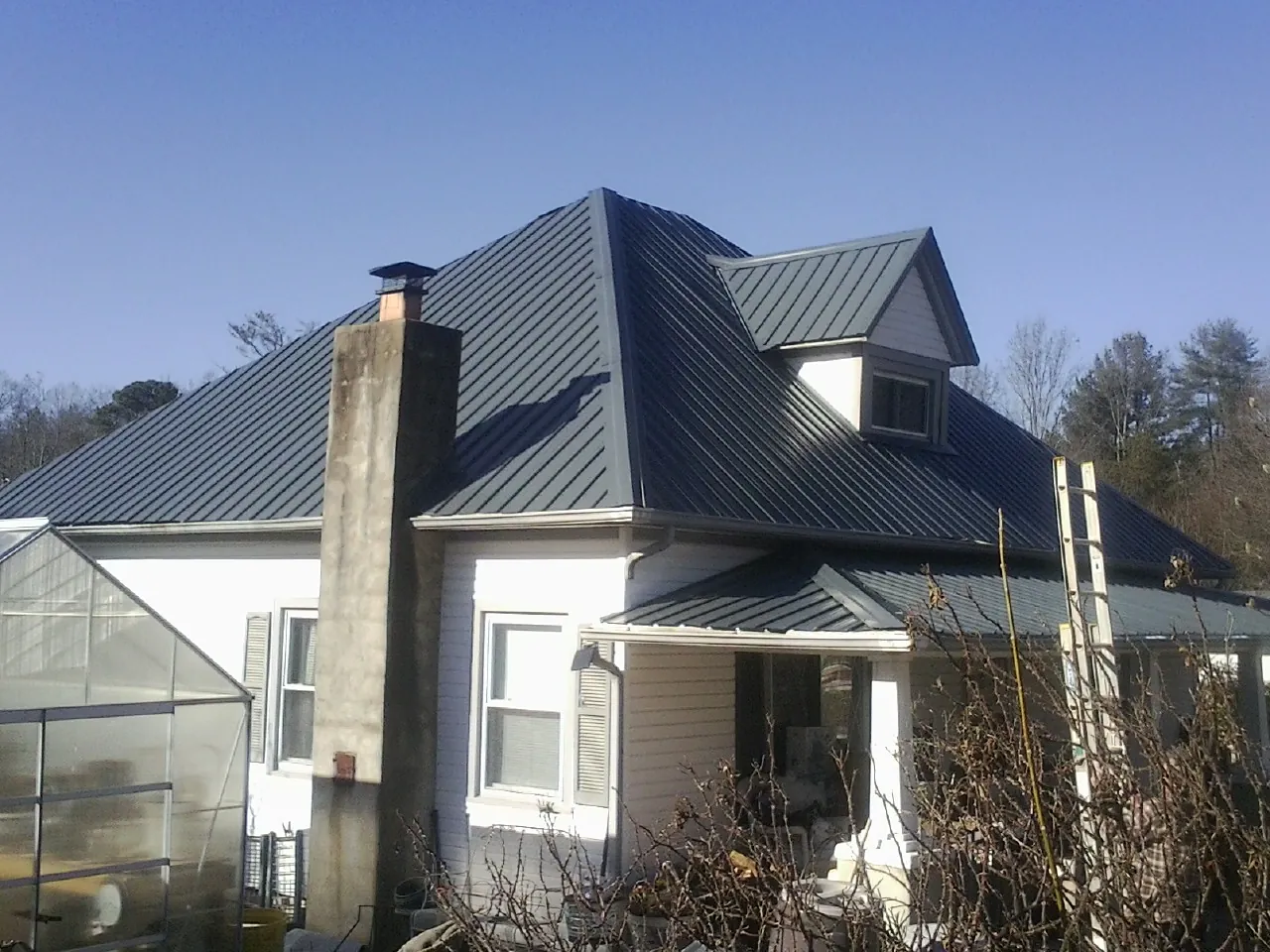 Dark blue standing seam metal roof on a white farmhouse with dormer — Slate & Tile Roof Repair by Roofing Brothers in Promise City