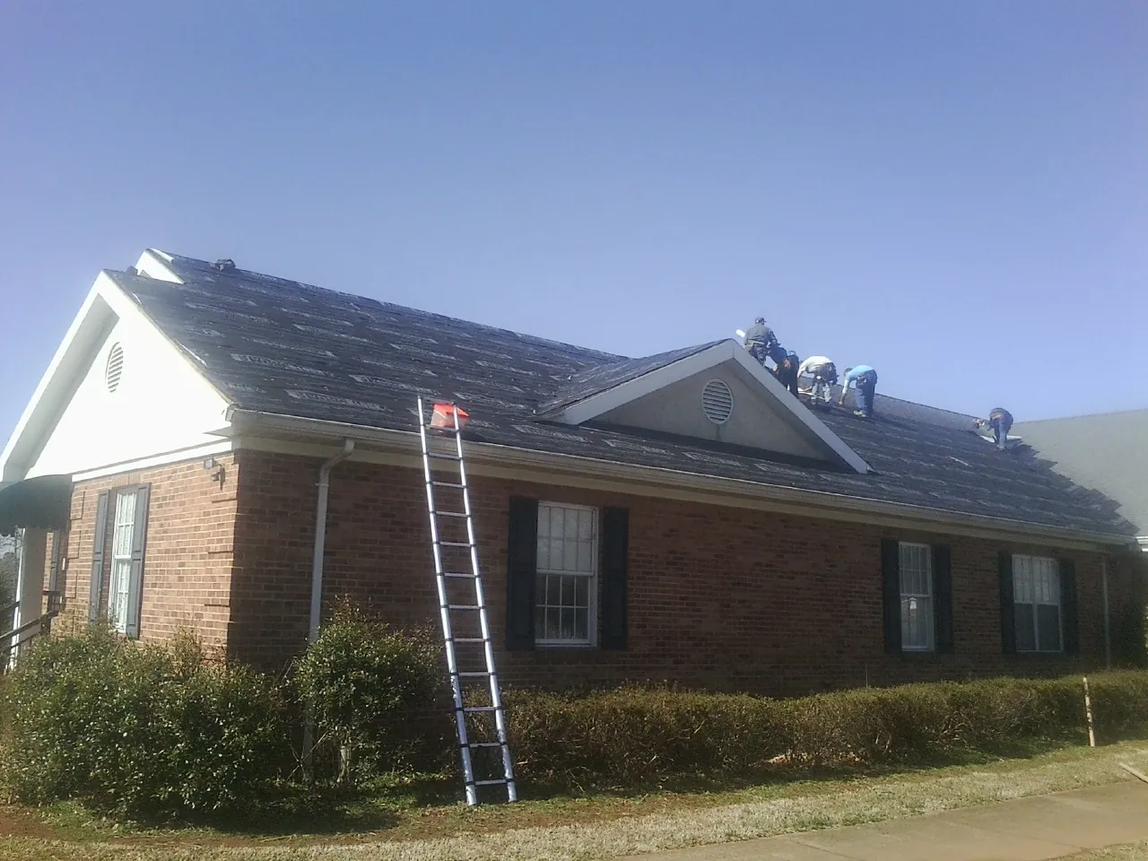 Crew tearing shingles off a brick ranch roof with a ladder set — Emergency Roof Repair work by our crew in Promise City