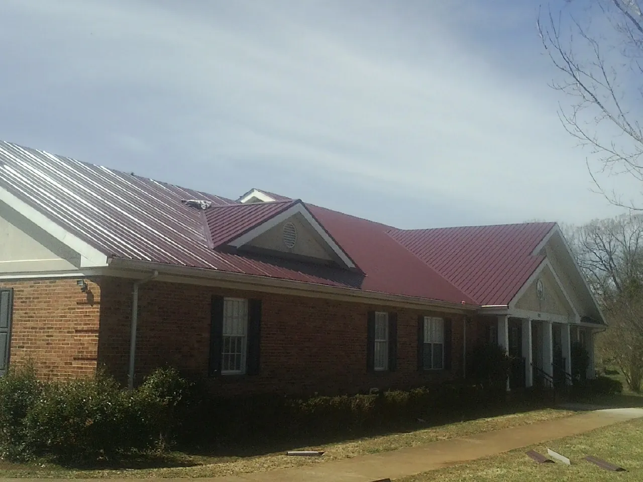 Red metal roof with gabled entries on a long brick building, from a Hail Damage Roof Repair job in Promise City