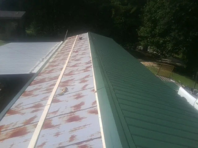 Old rusted panels beside newly installed green metal roofing — Wind Damage Roof Repair by Roofing Brothers in Promise City