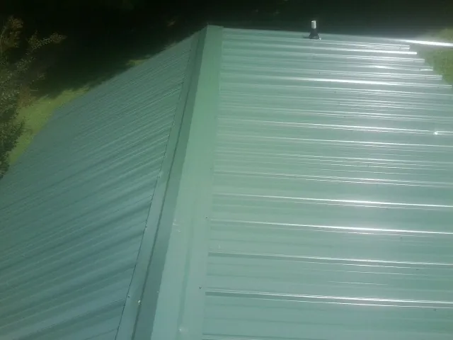 New green metal panels meeting at the ridge of a roof — Flat Roof Repair work by our crew in Promise City