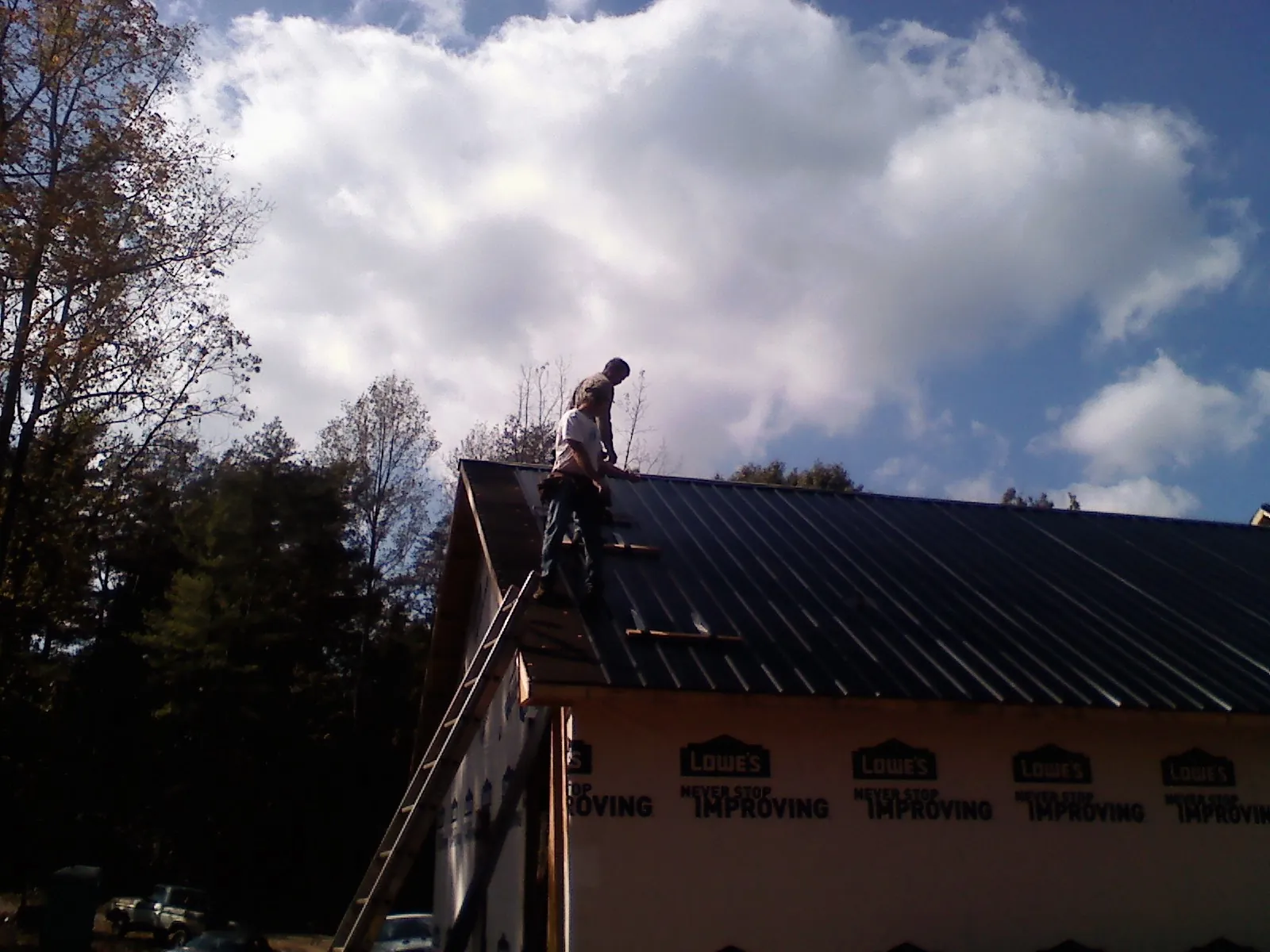 Roofer fastening dark metal panels high against a cloudy sky, from a Roof Inspection job in Promise City