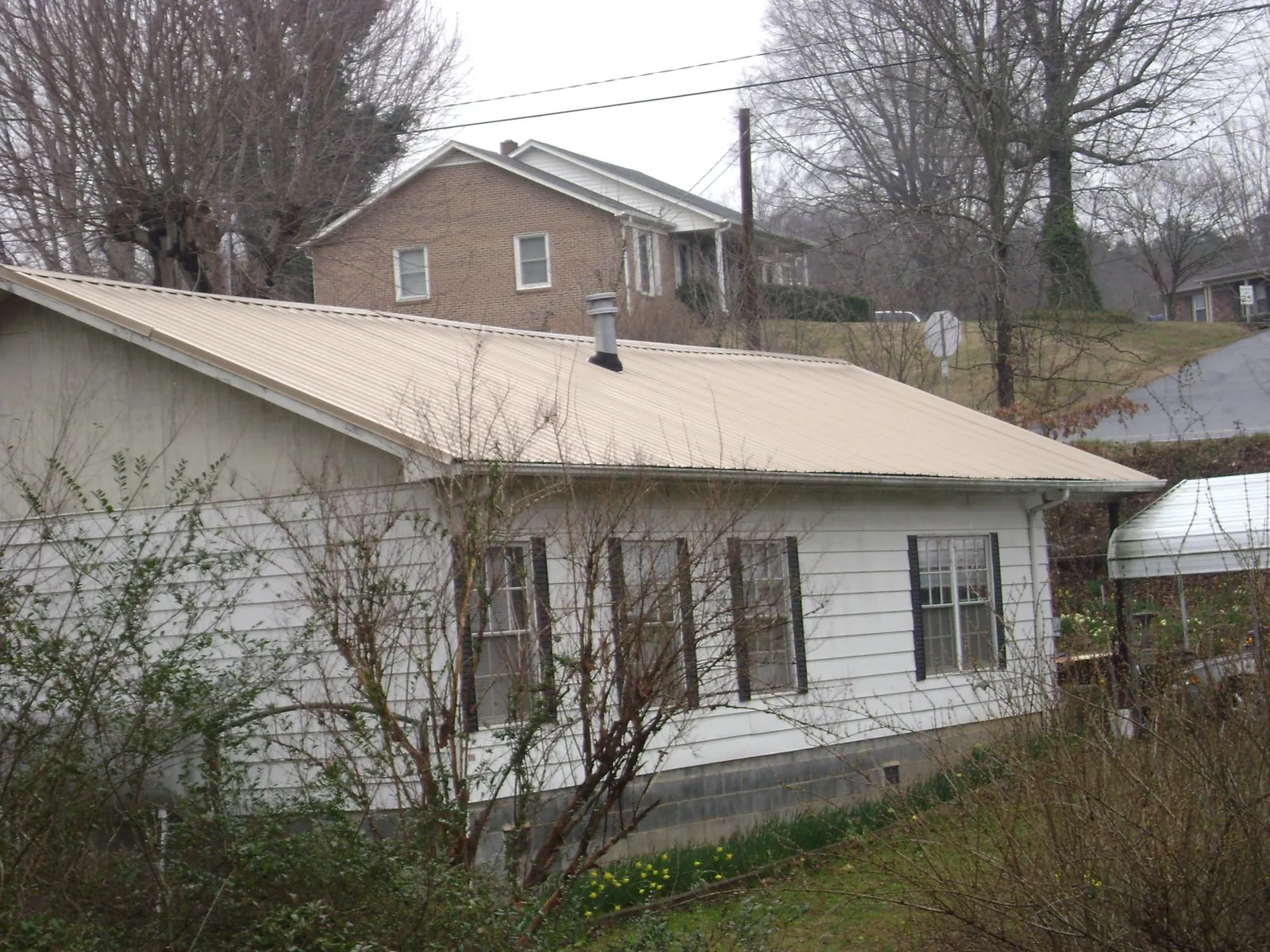 Tan metal roof on a white sided house set into a hillside — Commercial Roofing by Roofing Brothers in Promise City