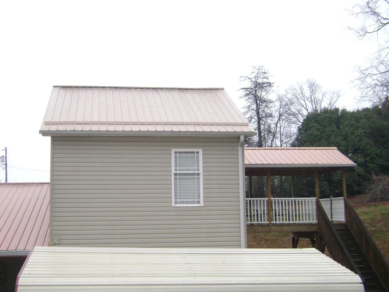 Tan metal roofs on a two story addition and attached porch, from a Roof Replacement job in Promise City
